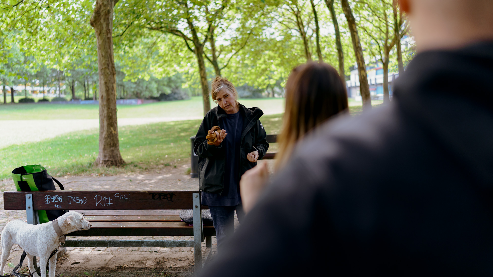 Maike ist über die Schultern von einem Kundenpaar zu sehen und erklärt ihnen etwas. Links von ihr steht einer ihrer Hunde.
