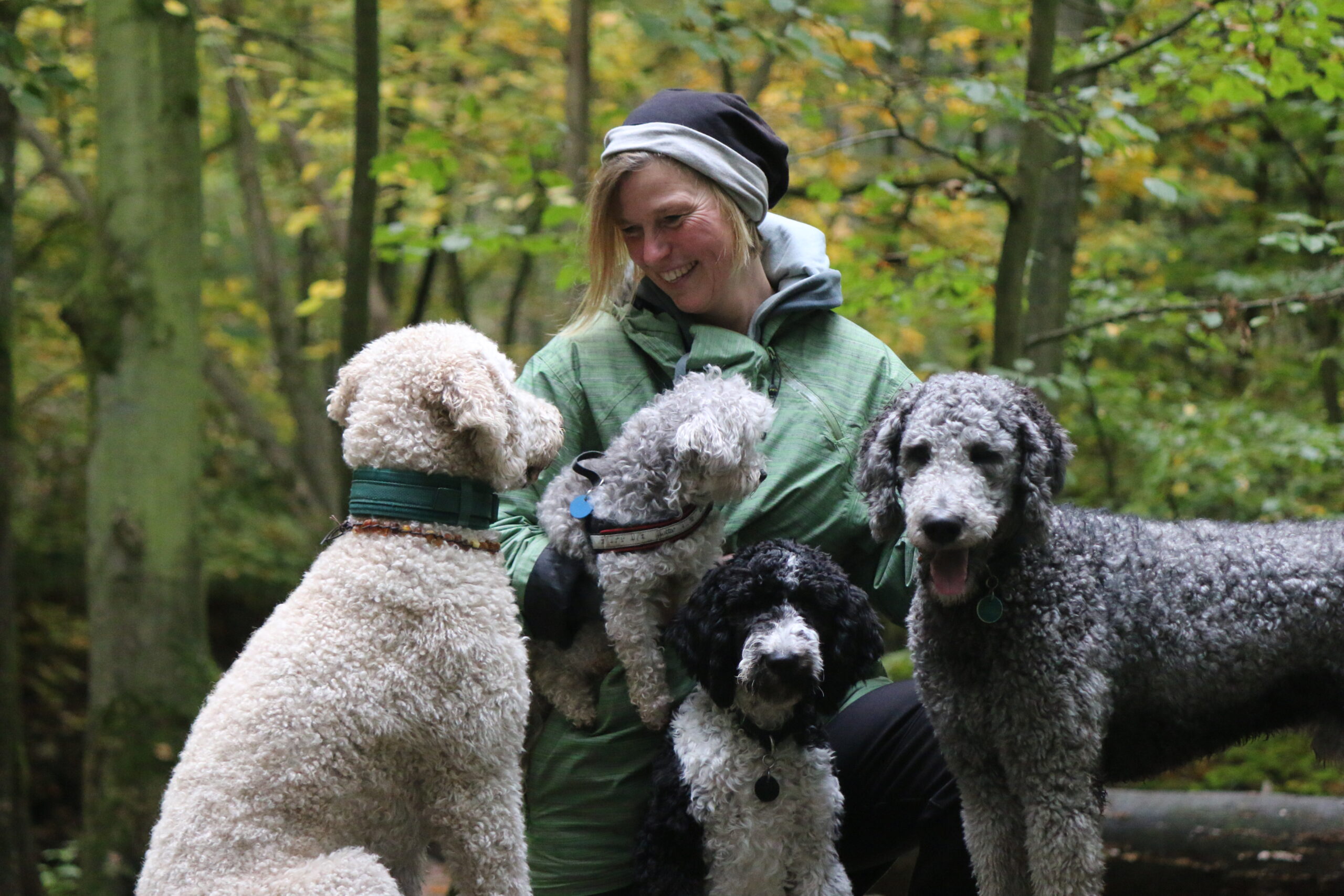 Maike mit ihren (früheren) Hunden. Mit einem sieht sie sich an, ein kleiner Hund ist auf ihrem Arm, zwei weitere dicht vor, neben ihr sehen in die Kamera